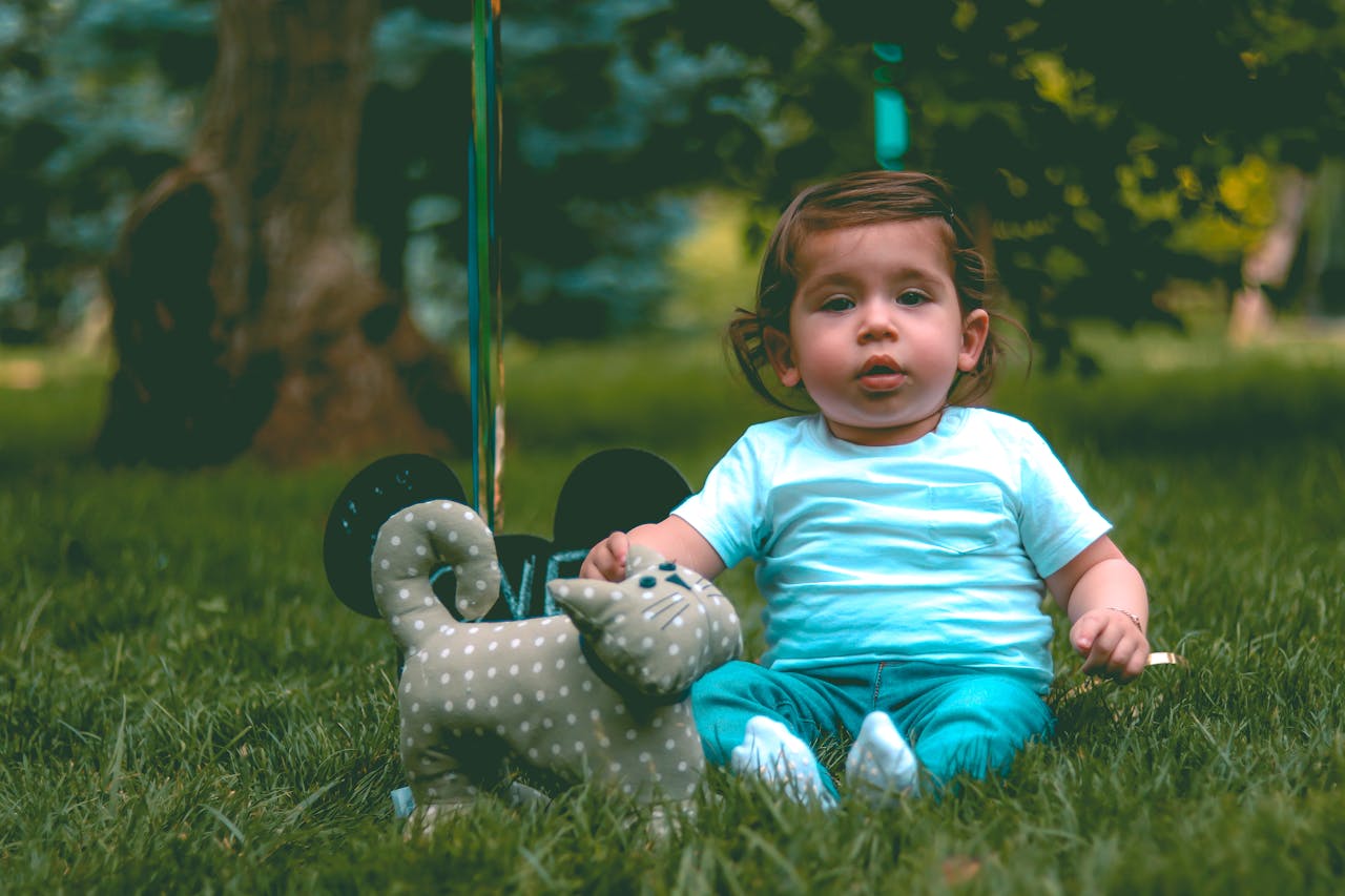 Cute baby sitting on grass with a toy cat in an outdoor park setting. Ideal for family and childhood themes.