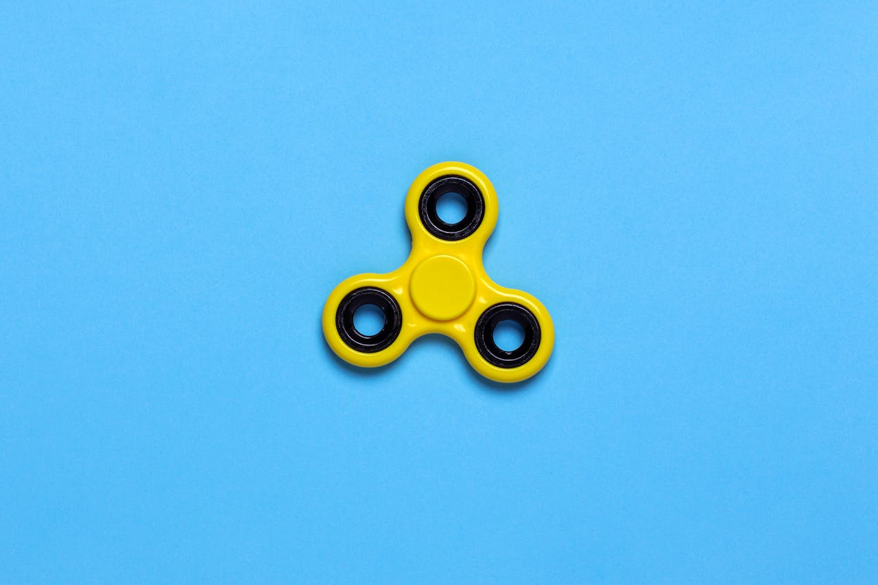 Close-up of a yellow fidget spinner on a vibrant blue background, perfect for design concepts.